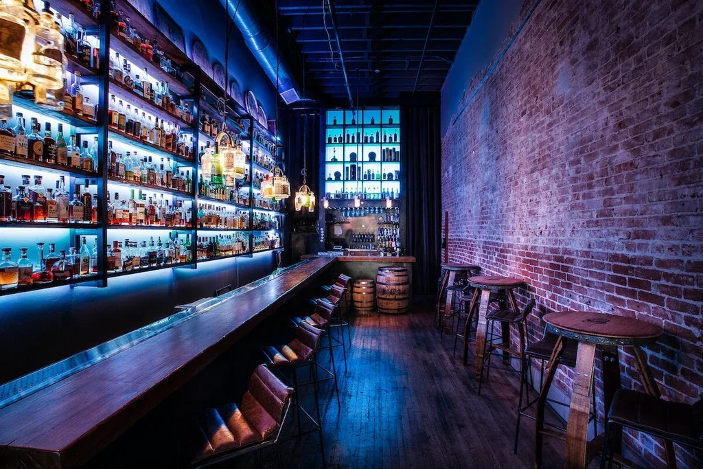 Upscale industrial bar with blue-lit bottles and a glowing brick wall.
