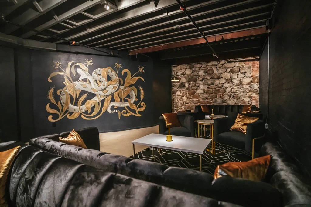 Dimly lit lounge featuring a snake mural, velvet seating, and industrial ceiling.