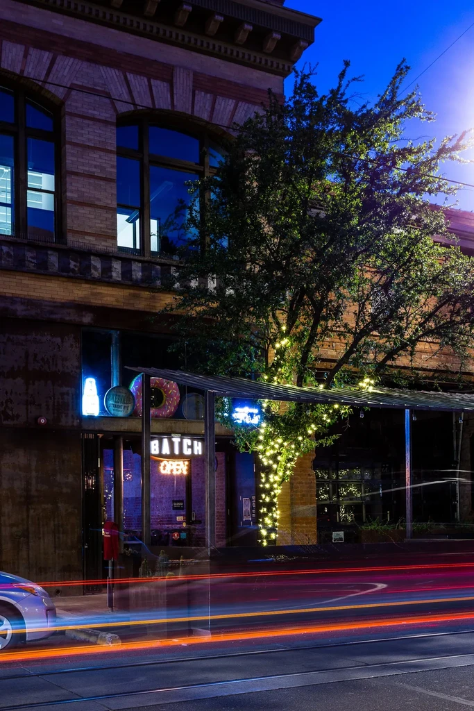 BATCH at night, multiple neon signs, lit tree, and street light trails.