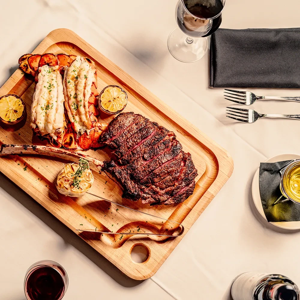Tomahawk steak, lobster tails, lemon, and wine on a luxurious table.