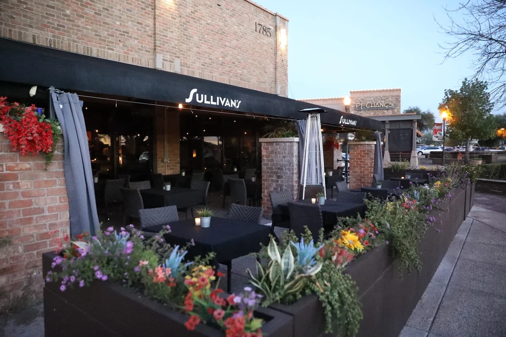 Sullivan's restaurant patio at dusk with string lights and colorful flowers.