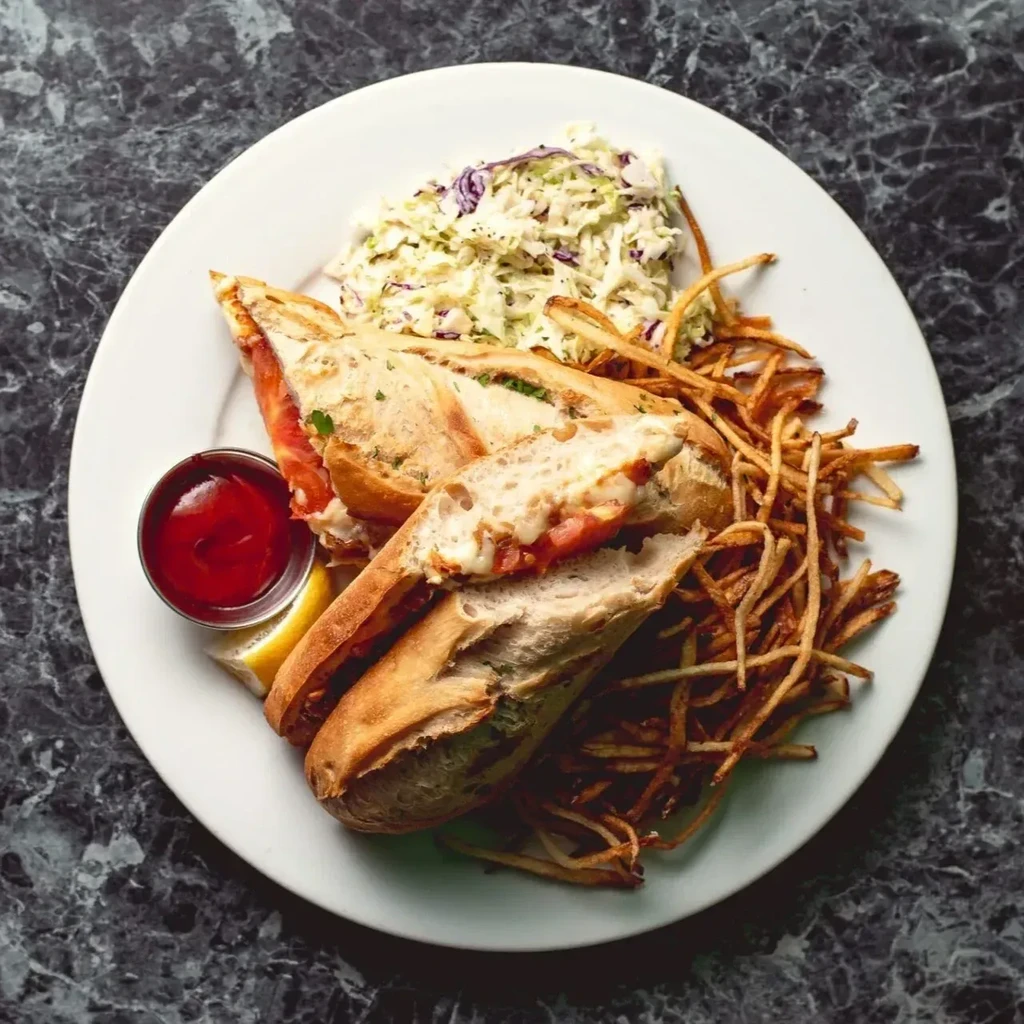 Sandwich, fries, coleslaw, ketchup, and lemon on a white plate.
