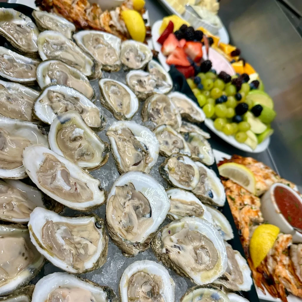 Plump shucked oysters on ice, with fruit and shrimp platter.