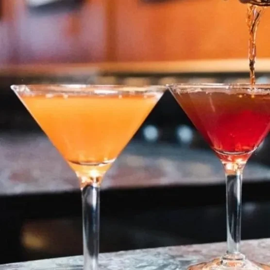 Two martini glasses, one red drink being poured, one orange.