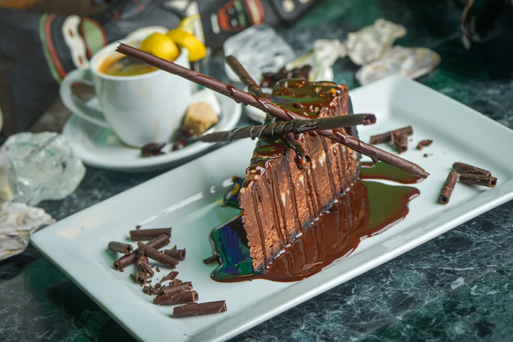 Chocolate cake slice with dripping sauce, chocolate decorations, and coffee cup.