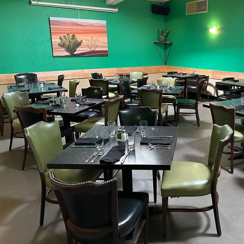 Green restaurant dining room with set tables and desert landscape decor.