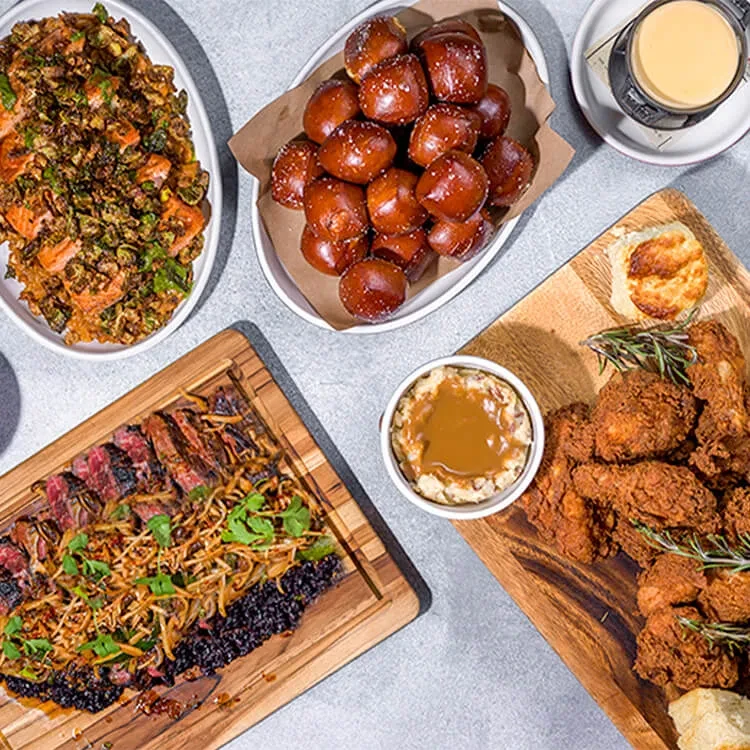 Overhead spread of baked fish, steak, fried chicken, pretzels, and sides.