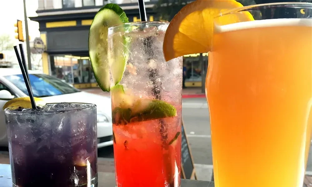 Three colorful drinks on an outdoor table, urban street background.