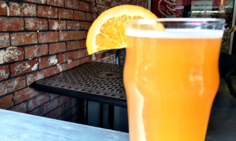 Orange drink with slice garnish, rustic brick wall, and table.