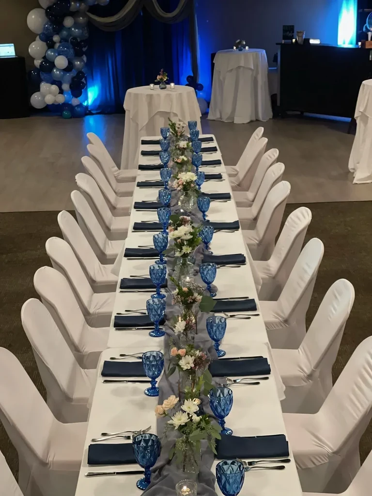 Meticulously set dining table with flowers, blue goblets, balloon arch.