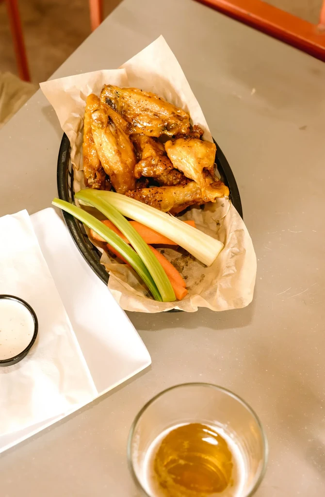 Overhead view of glazed chicken wings, vegetables, dip, and drink.