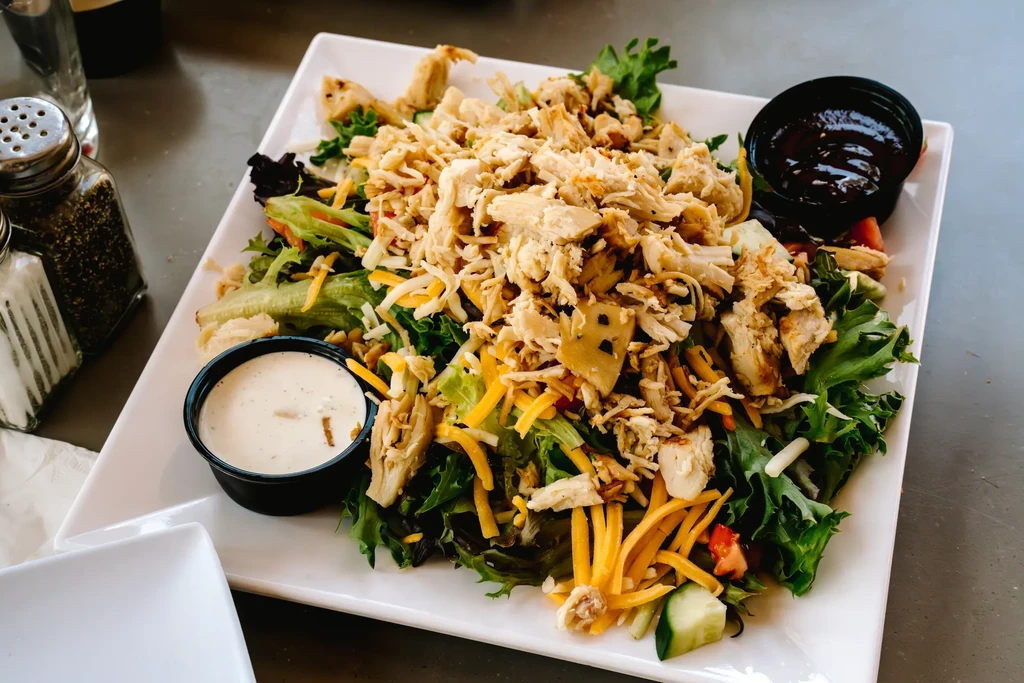 Large chicken salad with cheese, tomatoes, cucumbers, and two dressings.