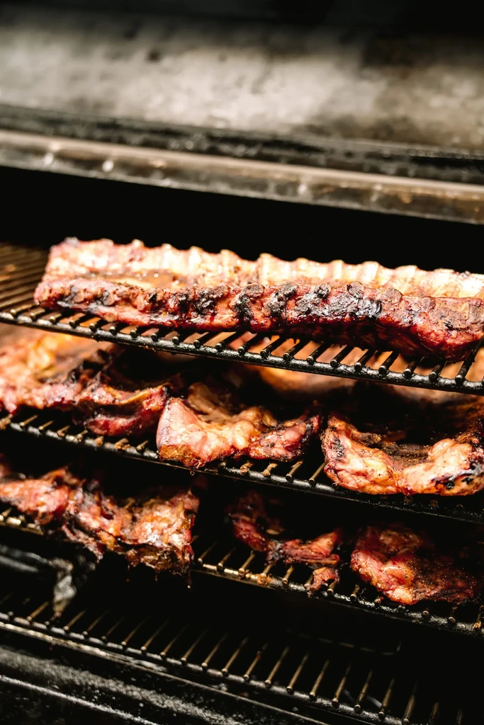 Cooked, charred ribs on grates within a large BBQ smoker.