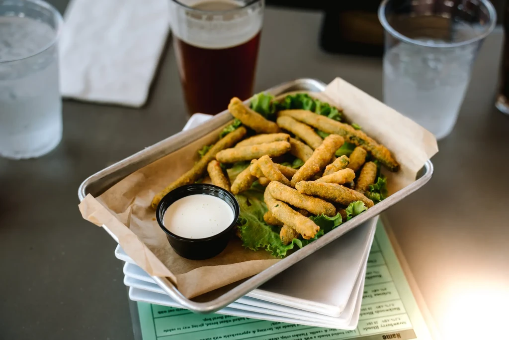 A serving of fried green beans with dipping sauce and drinks.