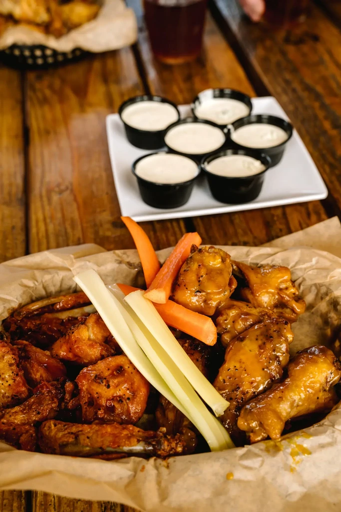 Basket of golden-brown chicken wings, celery, carrots, and dipping sauces.