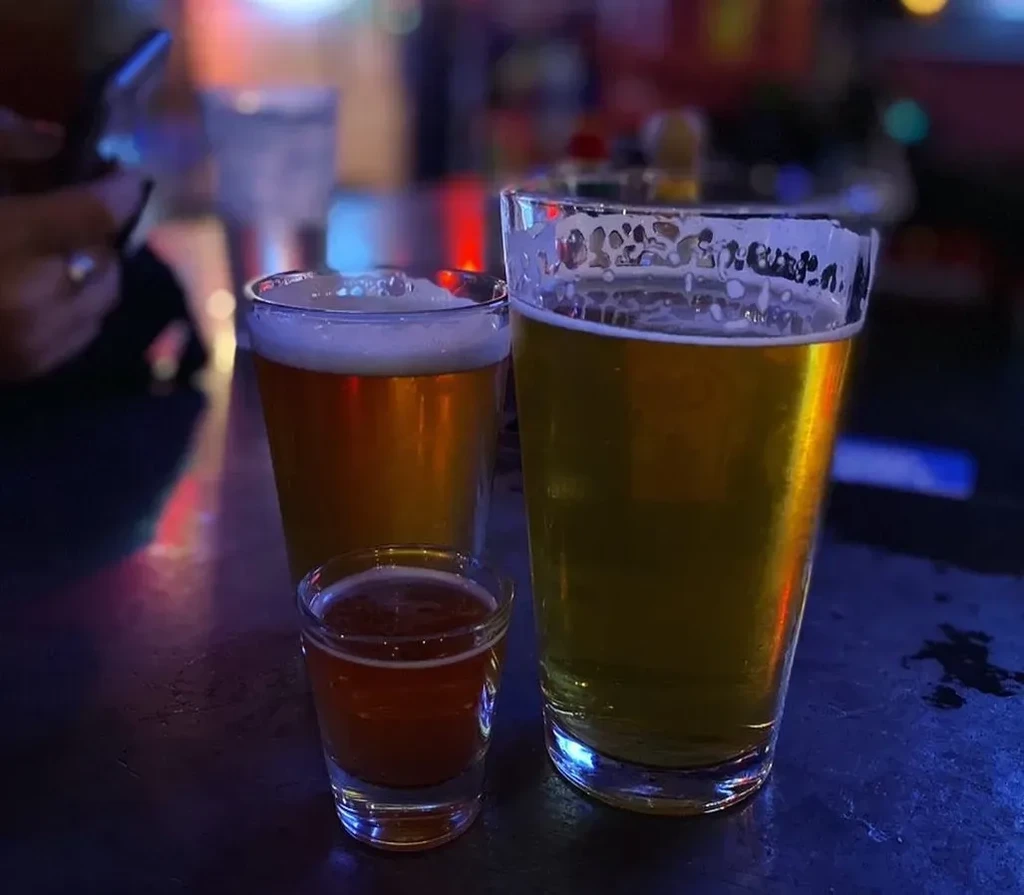 Three amber drinks, two pints and a shot, on a reflective bar.