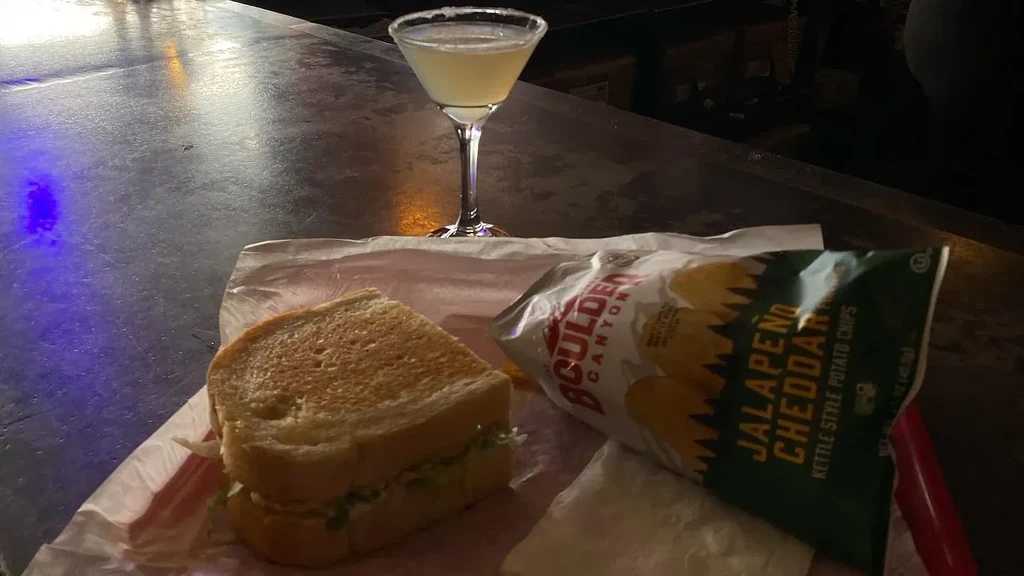 Toasted sandwich, jalapeño cheddar chips, and margarita in dimly lit bar.