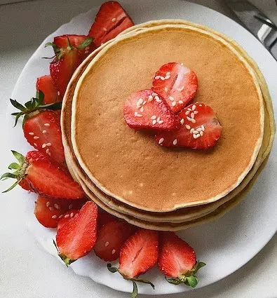 Stack of golden-brown pancakes with fresh strawberries and sesame seeds.