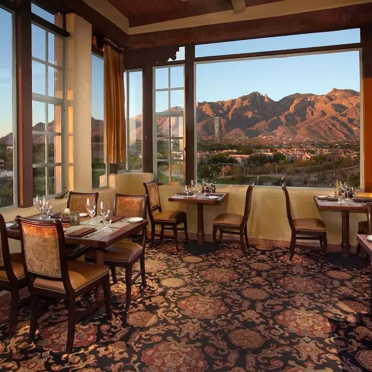 Elegant restaurant interior with set tables and panoramic mountain sunset view.