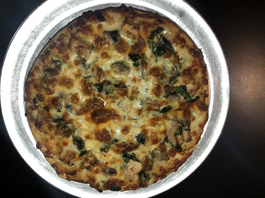 Close-up of baked chicken, spinach, and cheese pizza in a metal pan.