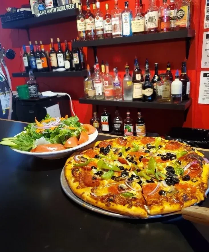 Pizza and salad on a counter with liquor bottles and a beer sign.