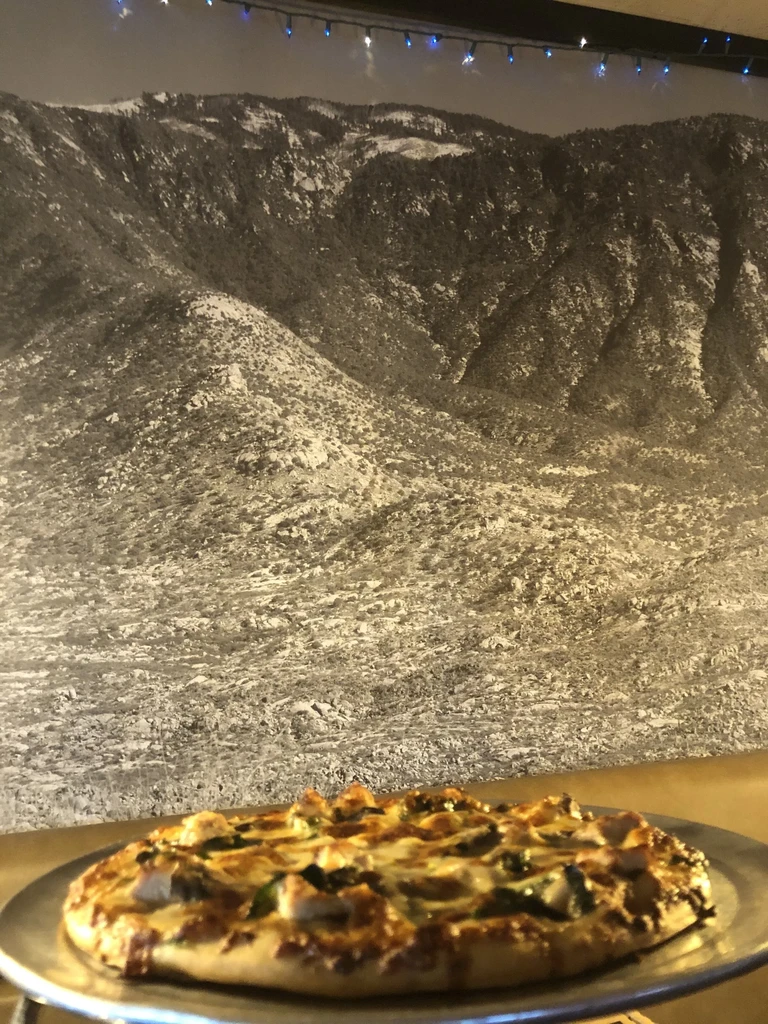 Close-up of chicken and greens pizza before a black and white mountain mural.