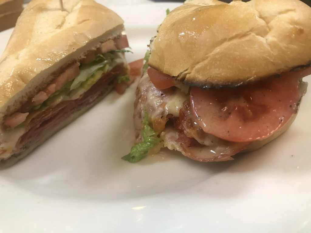 Two sandwiches: a sub and a toasted bun with meat, cheese, and vegetables.
