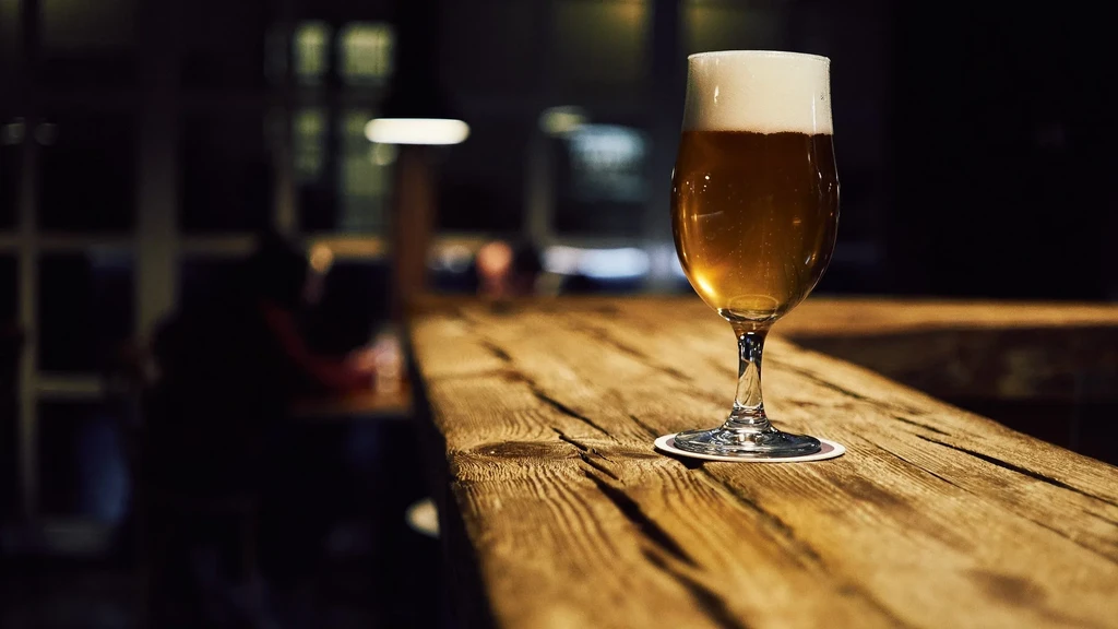 Golden beer with frothy head on rustic wooden bar, blurred background.