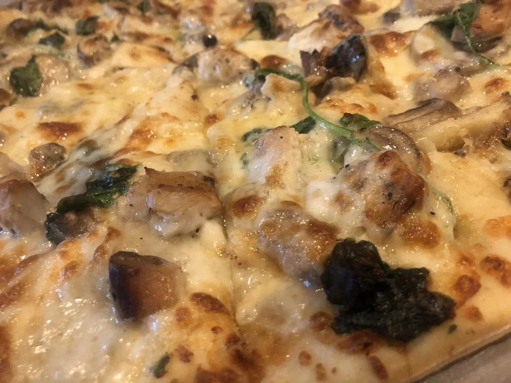 Close-up of freshly baked pizza with cheese, chicken, mushrooms, and greens.