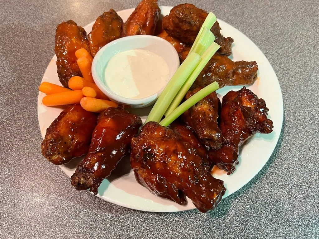 White plate of sauced chicken wings, carrots, celery, and dip.