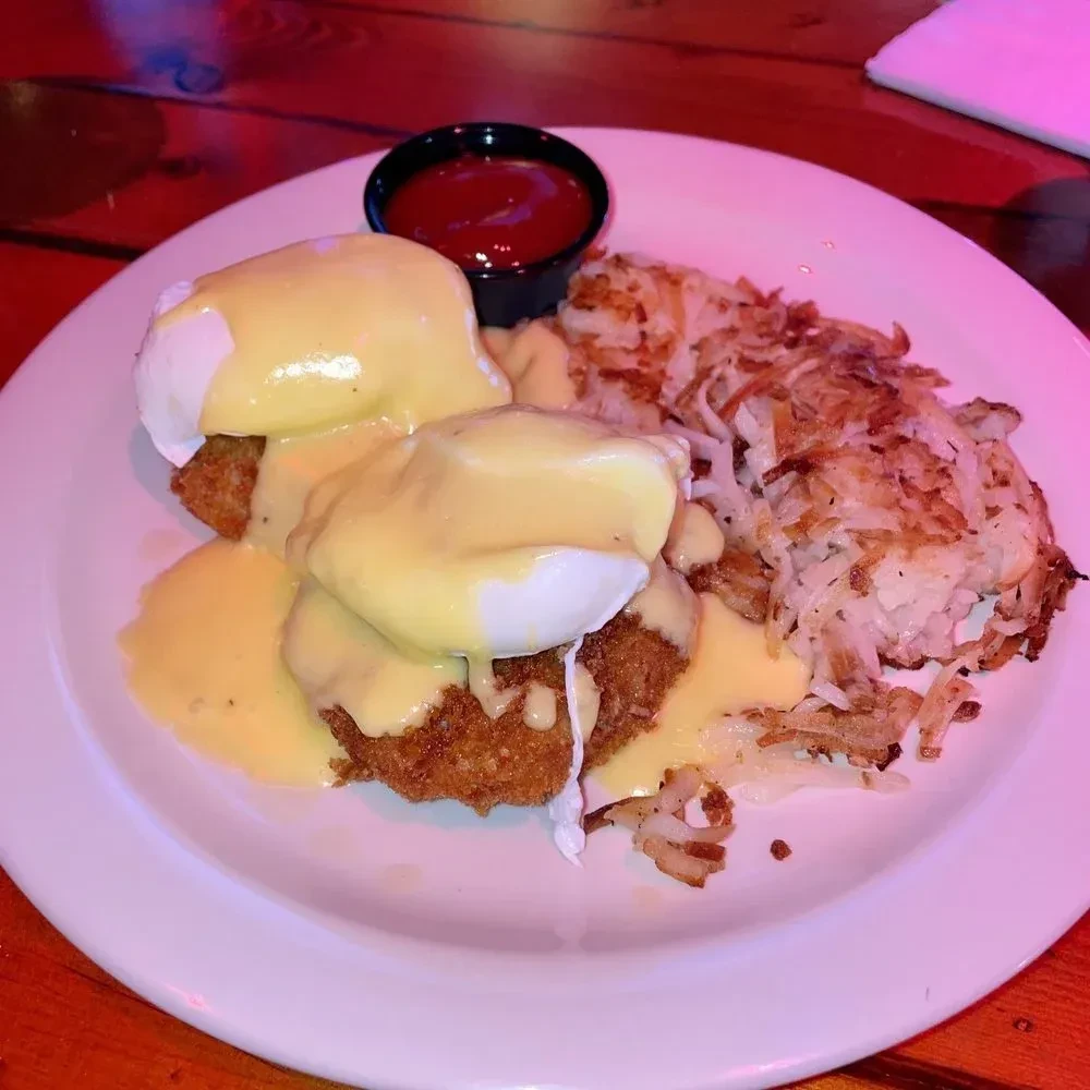 Close-up of eggs benedict style dish with hash browns and ketchup.