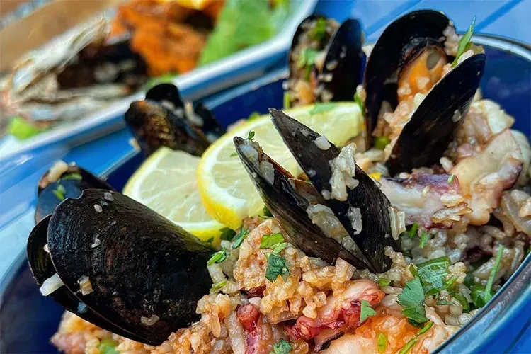 Close-up of seafood paella with mussels, octopus, lemon, and herbs.