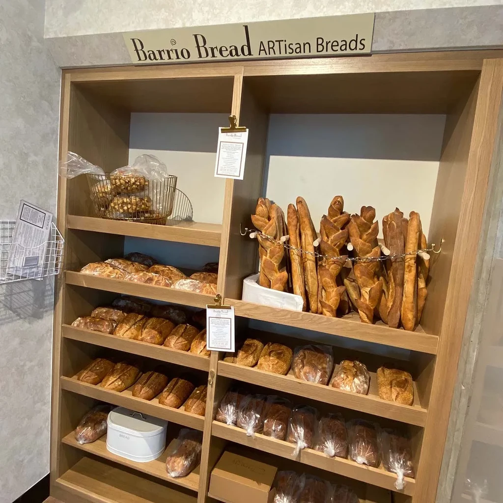 Wooden shelves display wrapped artisan breads, baguettes, and pastries.