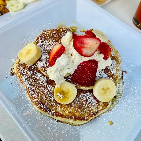 Two pancakes with whipped cream, strawberries, bananas, powdered sugar, and syrup.