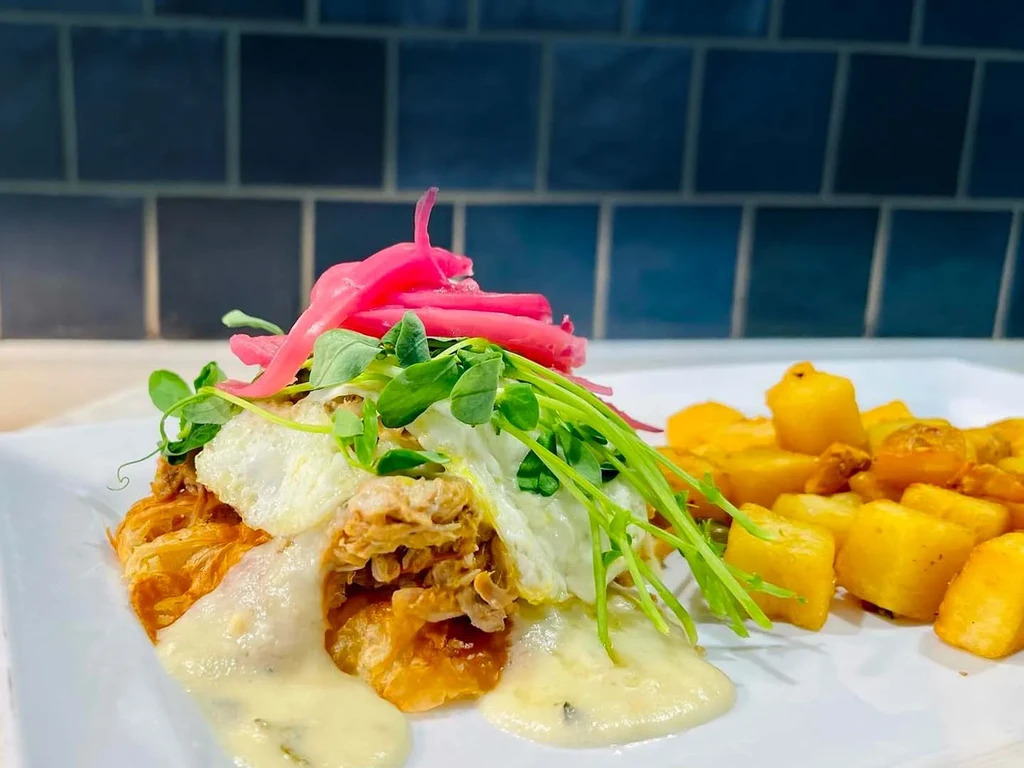 Plated savory meat, fried egg, sauce, microgreens, pickled onions, and potatoes.