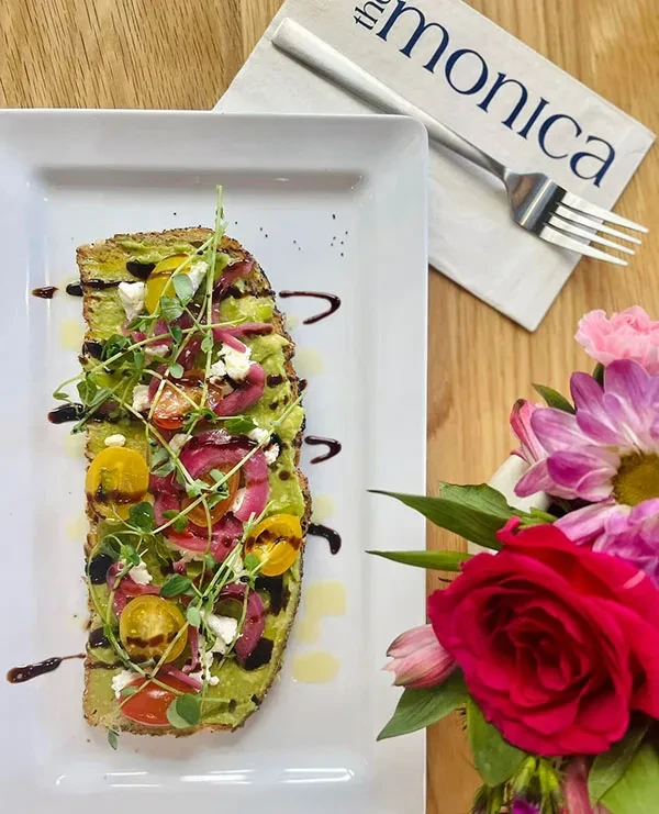 Overhead: gourmet avocado toast with avocado, tomatoes, cheese, microgreens, and flowers.