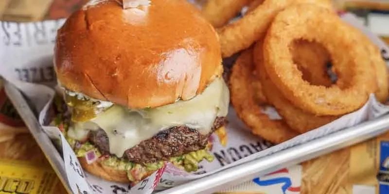 Gourmet burger, avocado, jalapeños, crispy onion rings on tray.