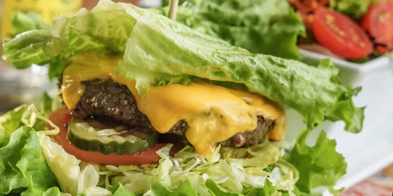 Close-up of a lettuce-wrap burger with cheese, patty, pickles, and tomato.