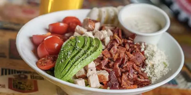 Close-up of a chicken salad with avocado, bacon, tomatoes, and dressing.