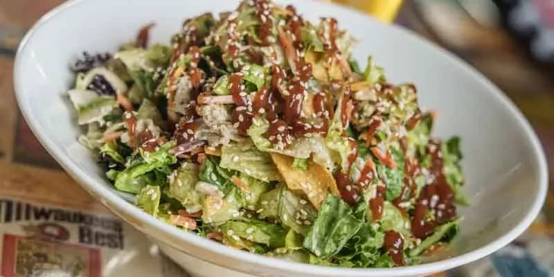 Chopped salad with dark sauce, sesame seeds, crispy elements in a bowl.