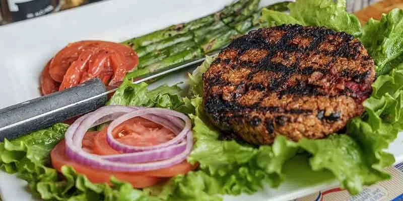 Charred burger patty with lettuce, tomato, onion, and asparagus.