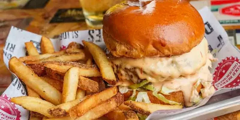 Large burger with creamy sauce, shredded lettuce, and seasoned fries in a tray.