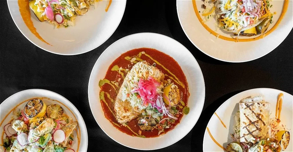 Top-down view of five artistically plated, diverse dishes on a dark surface.