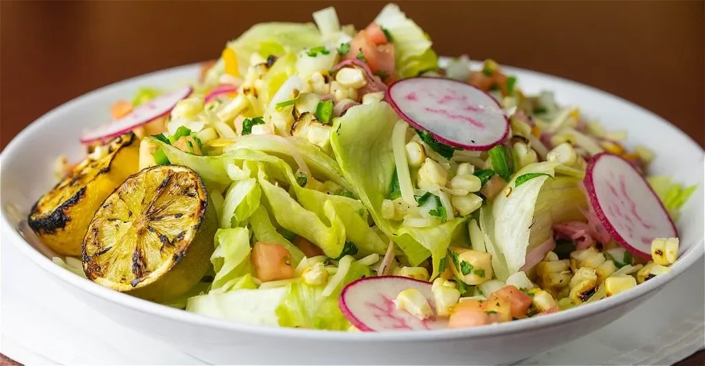 Colorful salad in a bowl with grilled corn, radishes, and charred limes.