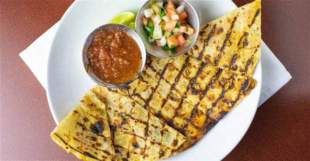 Grilled quesadilla pieces with salsa, pico de gallo, and lime wedges.