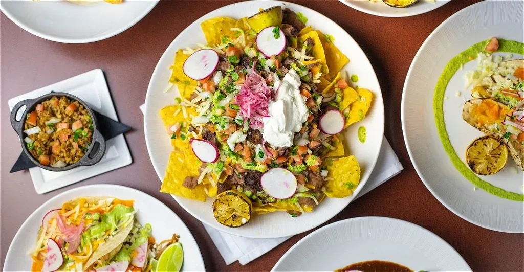 Overhead view of generously topped meat nachos and other Mexican dishes.