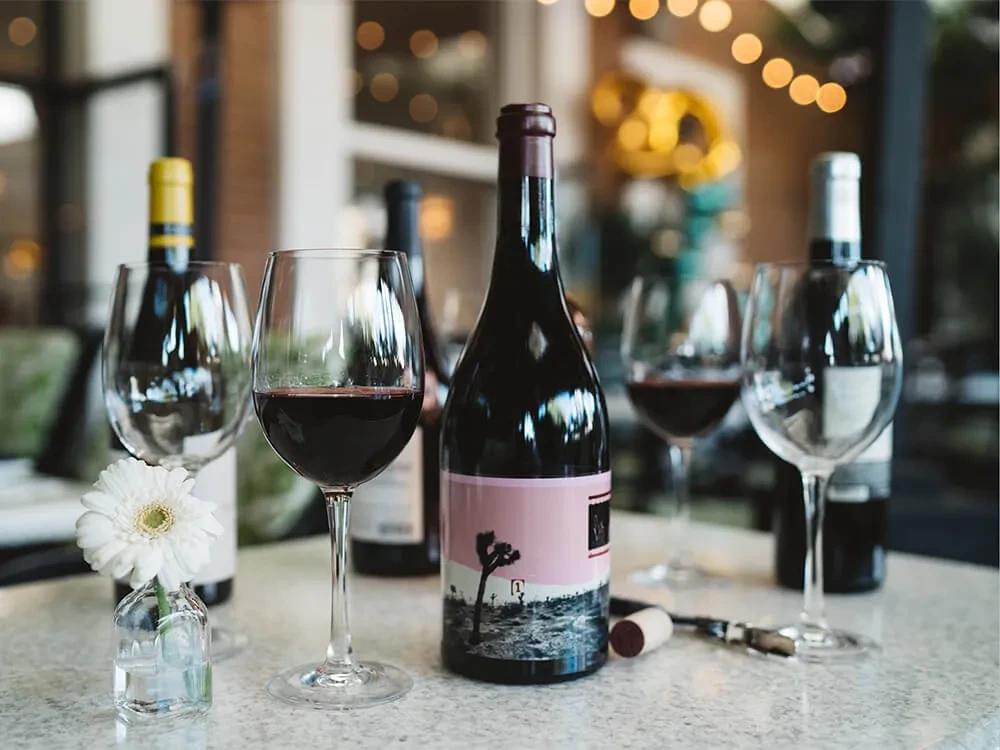 Dark wine bottle, red wine glass, daisy, and corkscrew on a table.