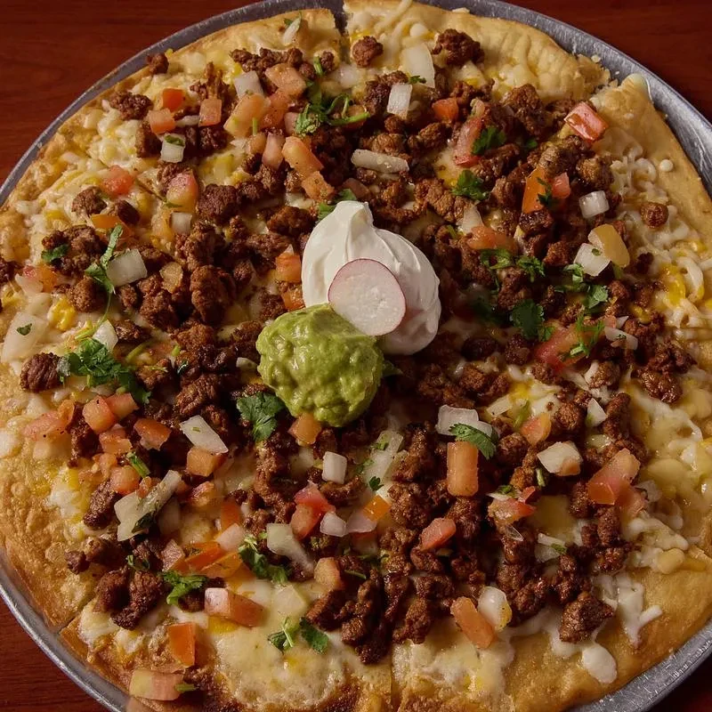 Taco pizza topped with meat, cheese, tomatoes, guacamole, and sour cream.