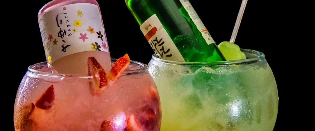 Pink and green cocktails with inverted bottles and fruit garnishes.