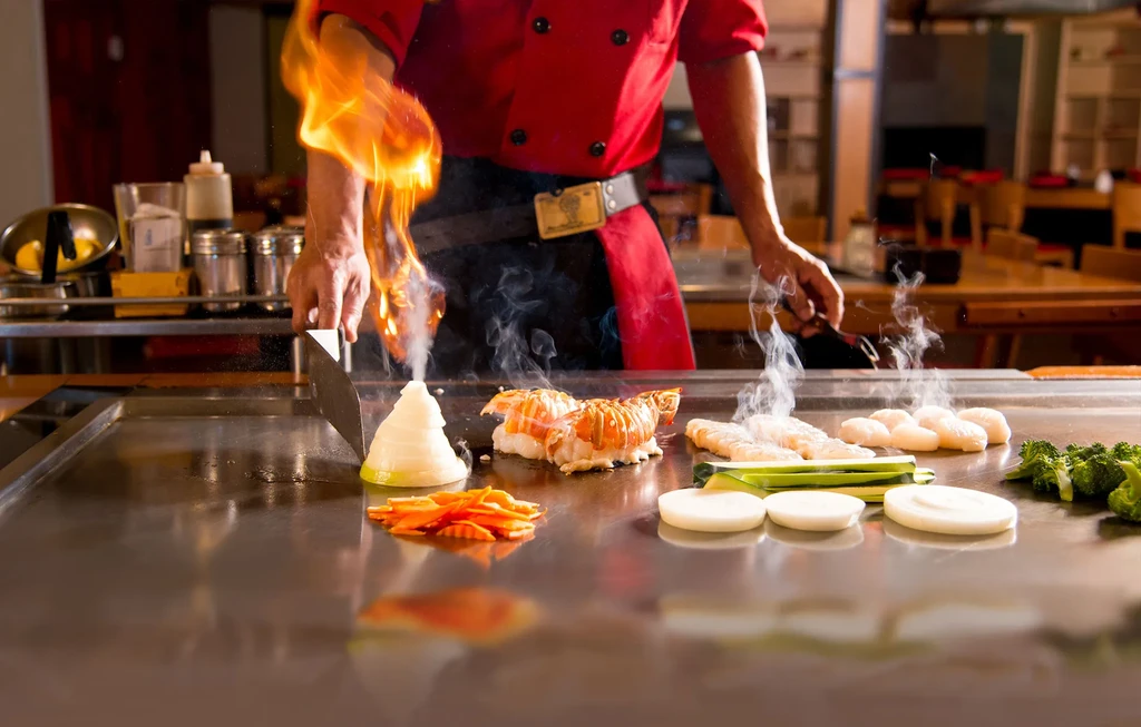 Chef cooking various foods on a teppanyaki grill with flaming onions.